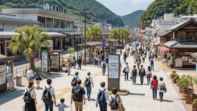 Cheerful daytime photo of Atami Station area with travelers walking calmly, signage visible, nearby streets leading toward the onsen town, coastal hills in the background. Clean, organized travel vibe, easy-to-understand location feeling, bright colors, natural light, friendly and beginner-friendly atmosphere.