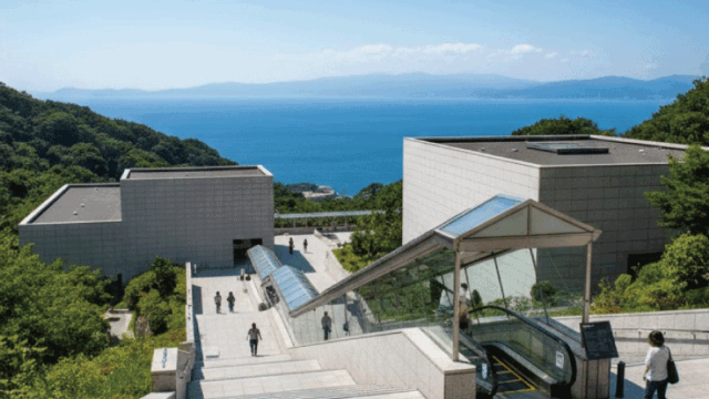 Bright daytime photo of MOA Museum of Art exterior or iconic entrance area with clean modern architecture, hillside setting, ocean view in the distance, clear sky. Realistic photography, inviting travel vibe, no close-up faces, fresh and approachable tone.