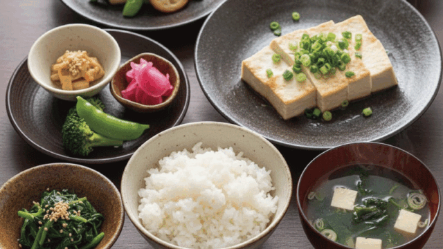 A beautifully arranged Japanese vegan meal.  Rice, tofu, vegetable side dishes, miso-style soup (plant-based), pickles.  Served on traditional Japanese tableware.  Top-down angle, natural lighting, realistic food photography, fresh and appetizing.