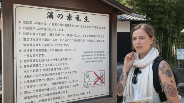 Bright and approachable photo style showing a foreign traveler looking slightly unsure while reading an onsen rule sign, mixed emotions of curiosity and concern, Japanese-style wooden signboard in background, calm setting, natural light, realistic candid travel photo, relatable and friendly tone