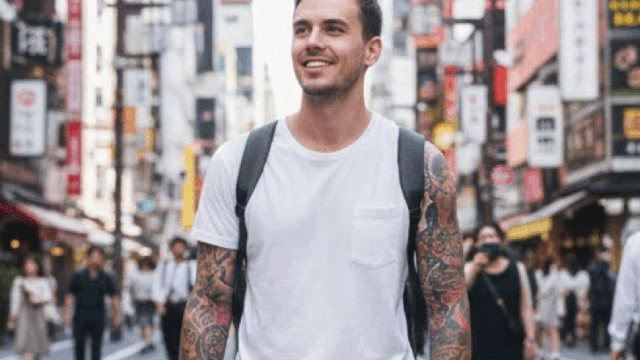 A relaxed foreign traveler with visible tattoos walking through a Japanese street, casual and confident, urban Japan background, realistic photography, bright daylight, friendly travel vibe